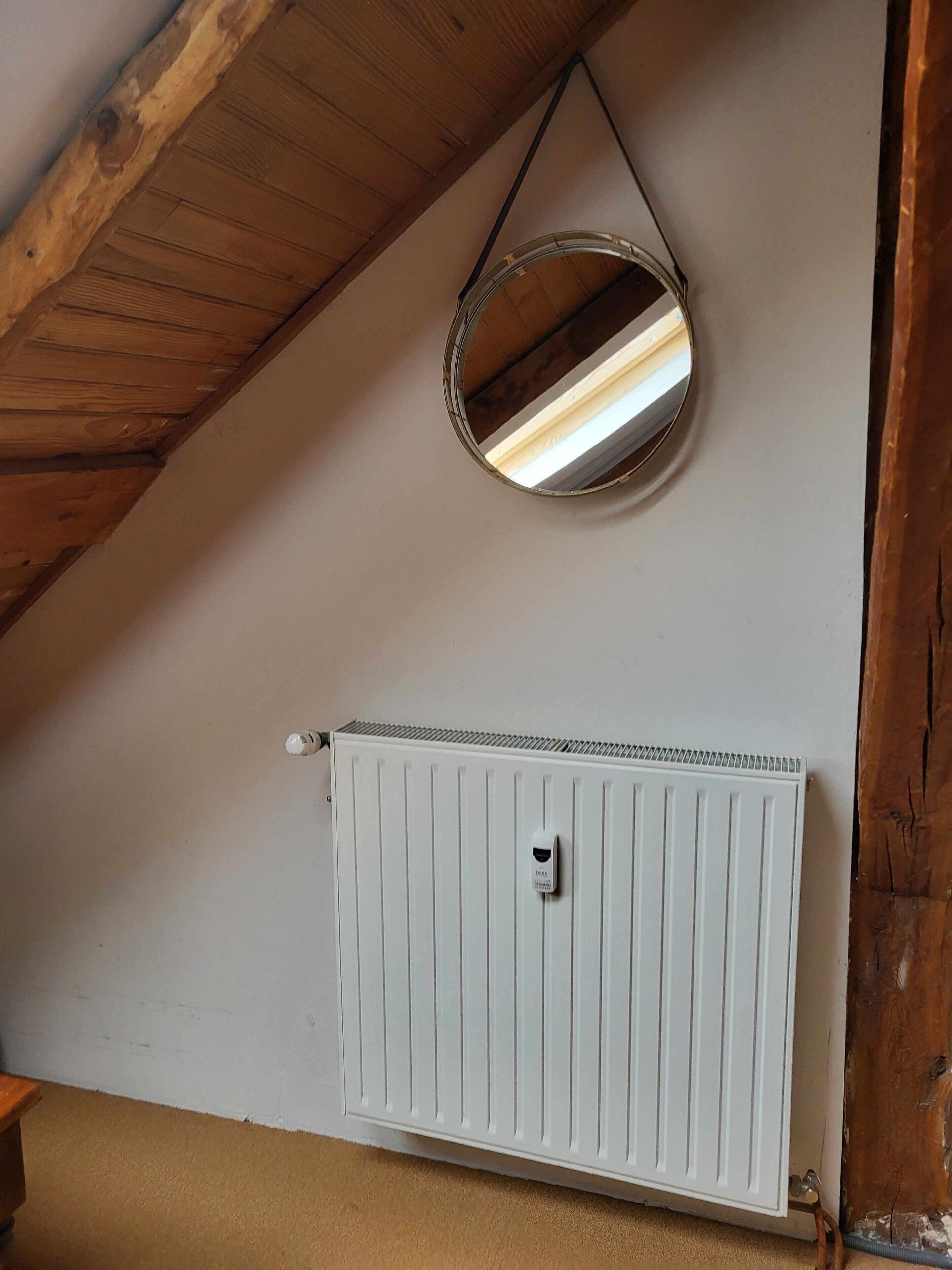 A room with a sloped ceiling, a white radiator, and a round mirror on the wall.