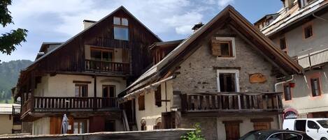 A traditional chalet-style building with a balcony, a car parked in front, and a clear sky.