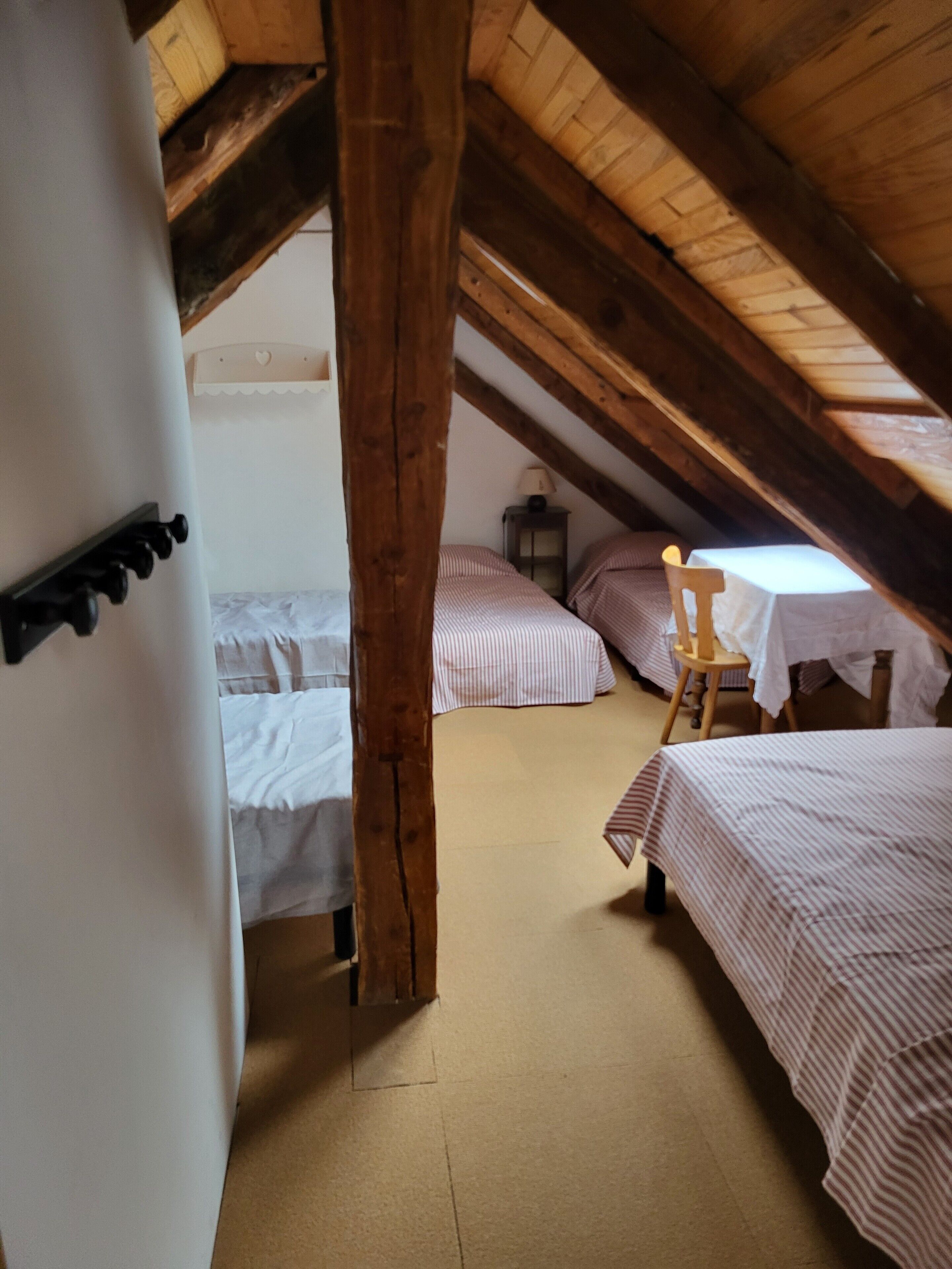 An attic bedroom with wooden beams, two beds with striped bedding, a small table, and a chair.