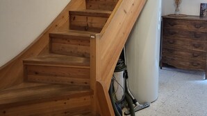 Una escalera de madera con barandilla, un espejo redondo en la pared y un aparador de madera con cajones.