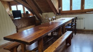 Una mesa de madera con bancos, una zona de cocina con estufa, y un ventanal con vistas a árboles.