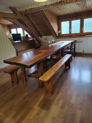 A wooden dining table with benches, a kitchen area with a stove, and a window with a view of trees.