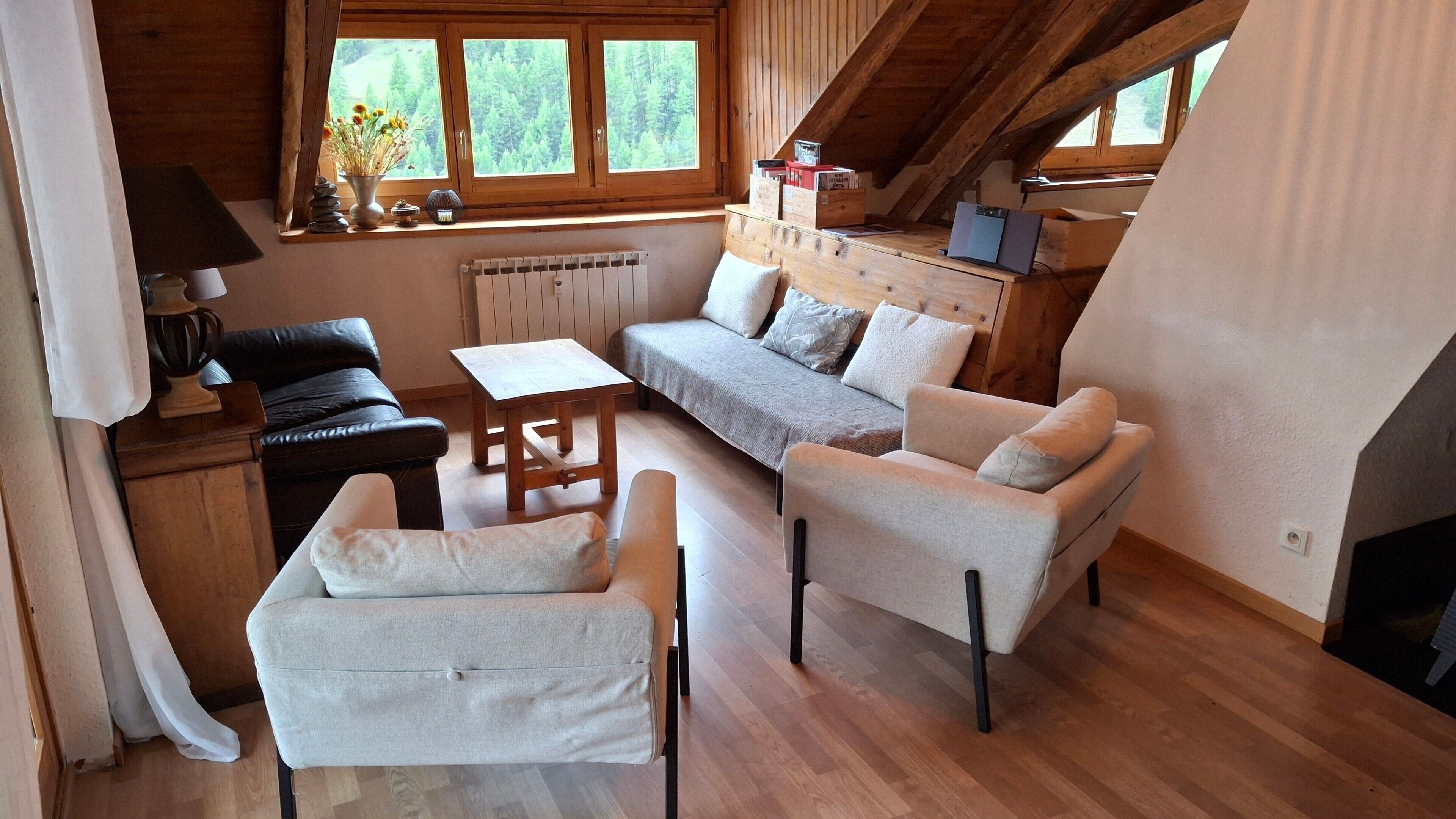 Une pièce confortable de style loft, avec un canapé, des fauteuils, une table et une vue sur une forêt grâce à de grandes fenêtres.