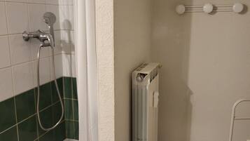 Et badeværelse med bruser, en radiator og en lille skammel.