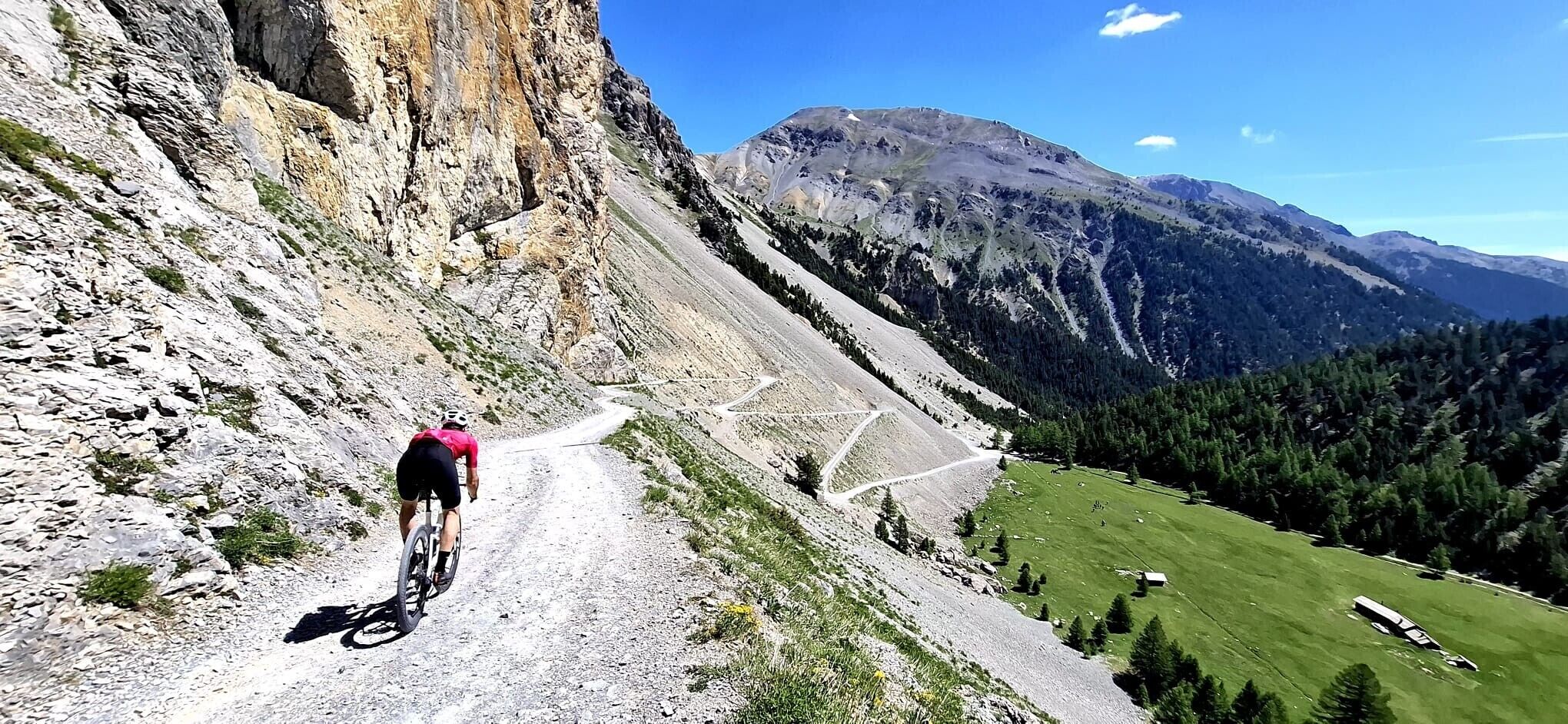 A mountain road with a cyclist, rocky terrain, and forested valley.