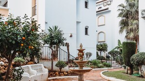 Un cortile con una fontana, posti a sedere bianchi all'aperto e un giardino curato.
