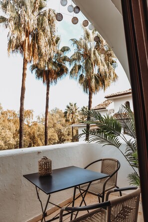 Een balkon met een tafel en stoelen, omringd door palmbomen en een witte muur.