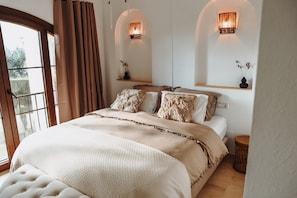 Ein Schlafzimmer mit einem großen Bett, einem Fenster mit Vorhängen und Wandleuchten.