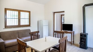 Een woonkamer met een bank, een eettafel met stoelen, een televisie, een open haard en een koelkast.