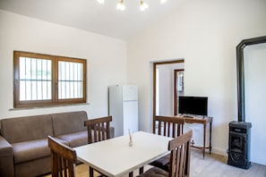 Uma sala de estar com sofá, mesa de jantar com cadeiras, televisão, lareira e frigorífico.