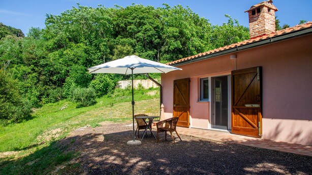 Een huis met een terras, een tafel met stoelen en een grote parasol.
