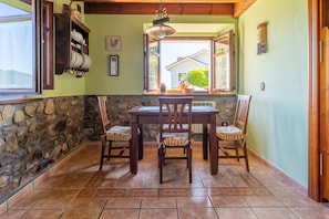 Un comedor con pared de piedra, mesa y sillas de madera, ventana con vistas, y una lámpara colgante.