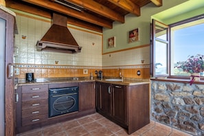Una cocina con armarios de madera, pared de piedra, ventana con vistas y salpicadero de azulejos.