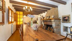 Un comedor con una larga mesa de madera, sillas, una araña y una chimenea de piedra.