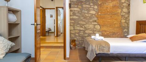 A bedroom with a stone wall, a wooden door, a bed, a bedside table, and a wardrobe.