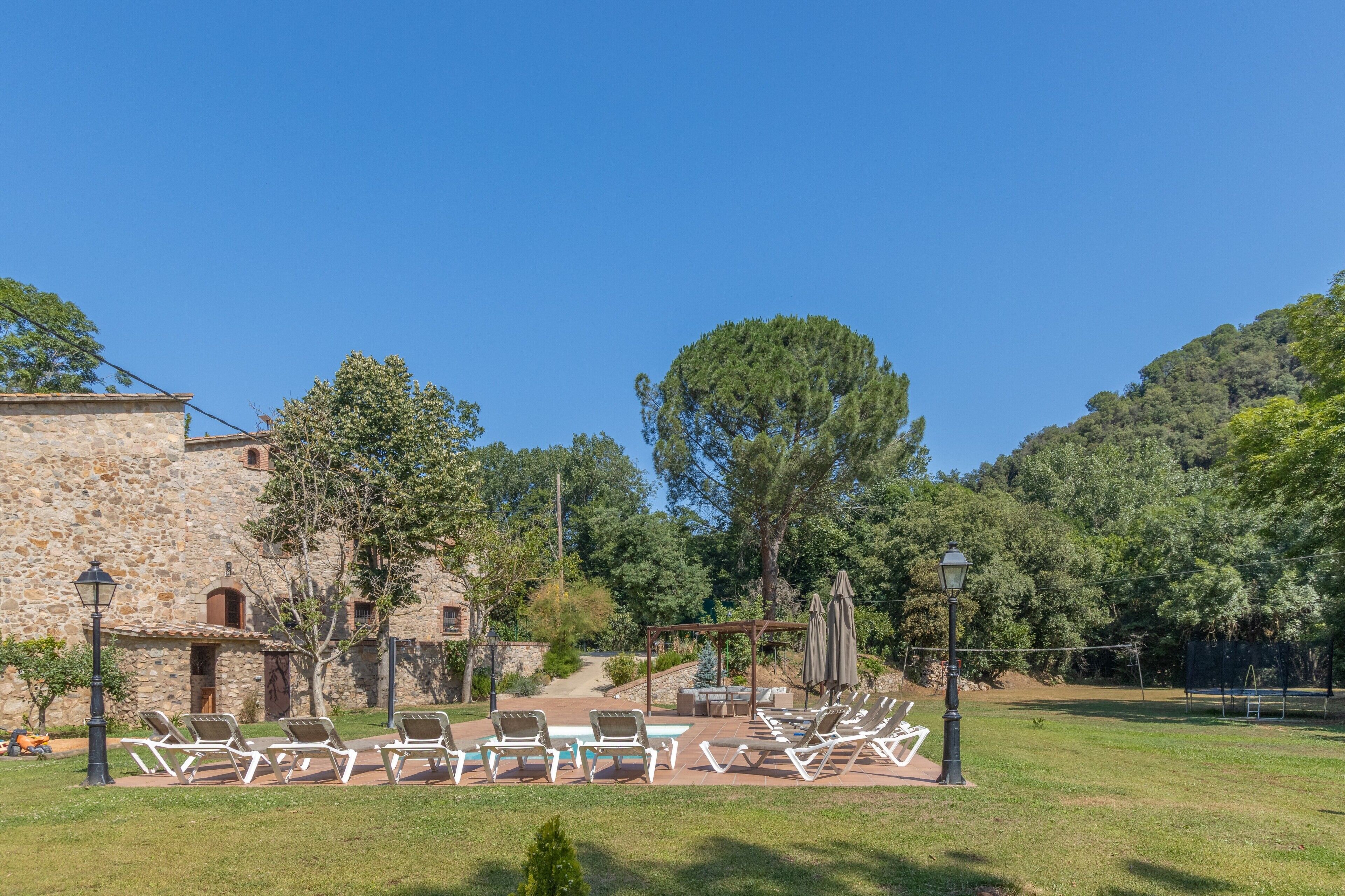 A stone building with a patio area featuring sun loungers and a pergola with umbrellas.