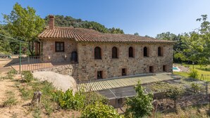 Un edificio de piedra con techo de tejas, ventanas en arco y un patio cercado.