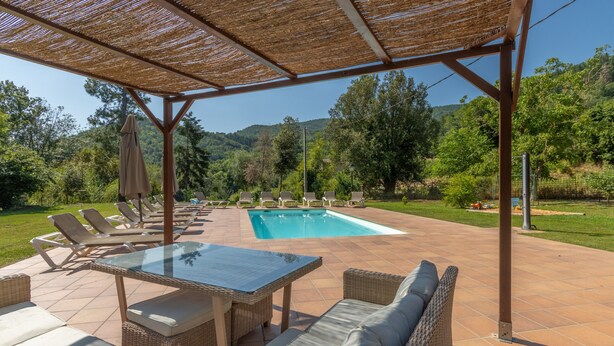 Un espacio al aire libre techado con piscina, sillones de descanso y una mesa.