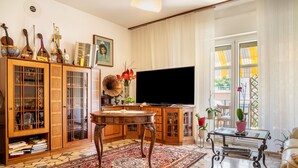 A living room with a TV, wooden cabinets, a patterned rug, and a glass coffee table. - Apartment 'Re 1' with Balcony, Wi-Fi and Air Conditioning (Trento)