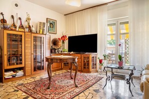 Ein Wohnzimmer mit Fernseher, Holzschränken, einem gemusterten Teppich und einem Glastisch.