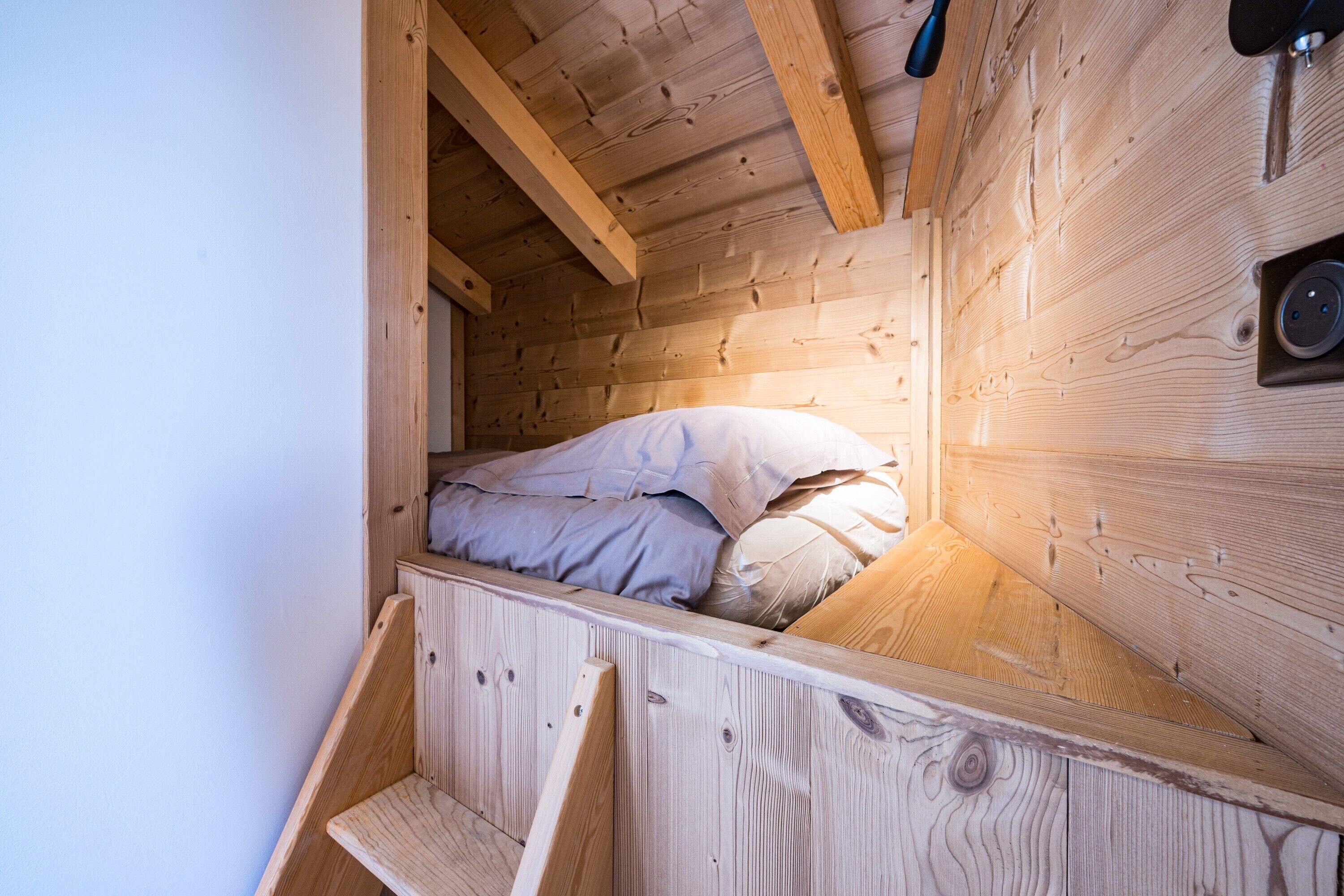 Eine Holzblockhütte mit Schlafkoje, einer kleinen Holzbank und einem an der Wand befestigten Lautsprecher.