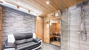 A modern interior with a black and white sofa, wooden walls, a glass shower enclosure, and a stone-tiled floor.