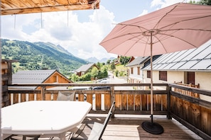 A wooden deck with a table and umbrella, overlooking a village with houses and mountains. - Apartment 'Le Crey Rond' with Mountain View, Private Terrace and Wi-Fi (Valloire)