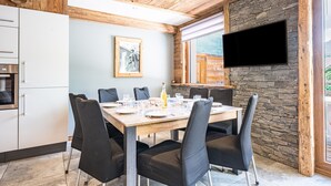 A dining area with a wooden table, black chairs, a stone wall, and a mounted TV.
