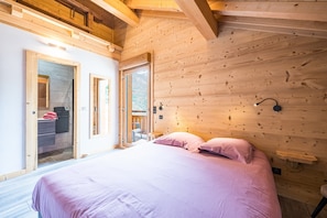 A bedroom with a bed, wooden walls, a window, and a door leading to a bathroom. - Apartment 'Le Crey Rond' with Mountain View, Private Terrace and Wi-Fi (Valloire)