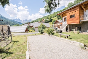 A rural mountain village with wooden houses, a gravel courtyard, and a mountain backdrop.