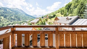 A wooden balcony overlooking a mountainous village with traditional houses and a car parked in front. - Apartment "Le Galibier" with Mountain View, Balcony and Wi-Fi (Valloire)