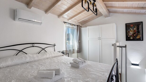 Ein Schlafzimmer mit Bett, weißen Wänden, einer Klimaanlage, einem Fenster mit Vorhängen, einem Kleiderschrank und einem Bild.