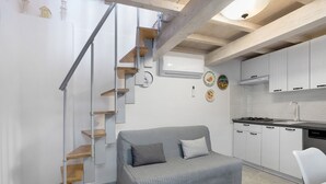 Ein kompakter Wohnraum mit grauem Sofa, einer Treppe, weißen Küchenschränken und einer kleinen Essecke.