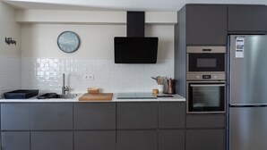 Eine moderne Küche mit Einbauofen, Mikrowelle, Edelstahlkühlschrank, Wanduhr und Spüle mit Wasserhahn.