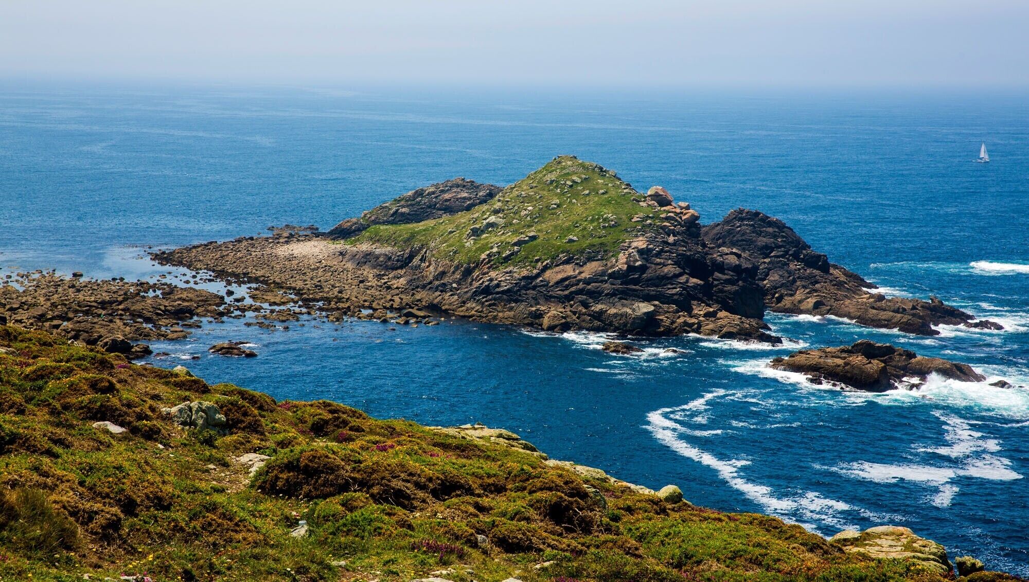 A rugged coastline with rocky outcrops and a small hill.
