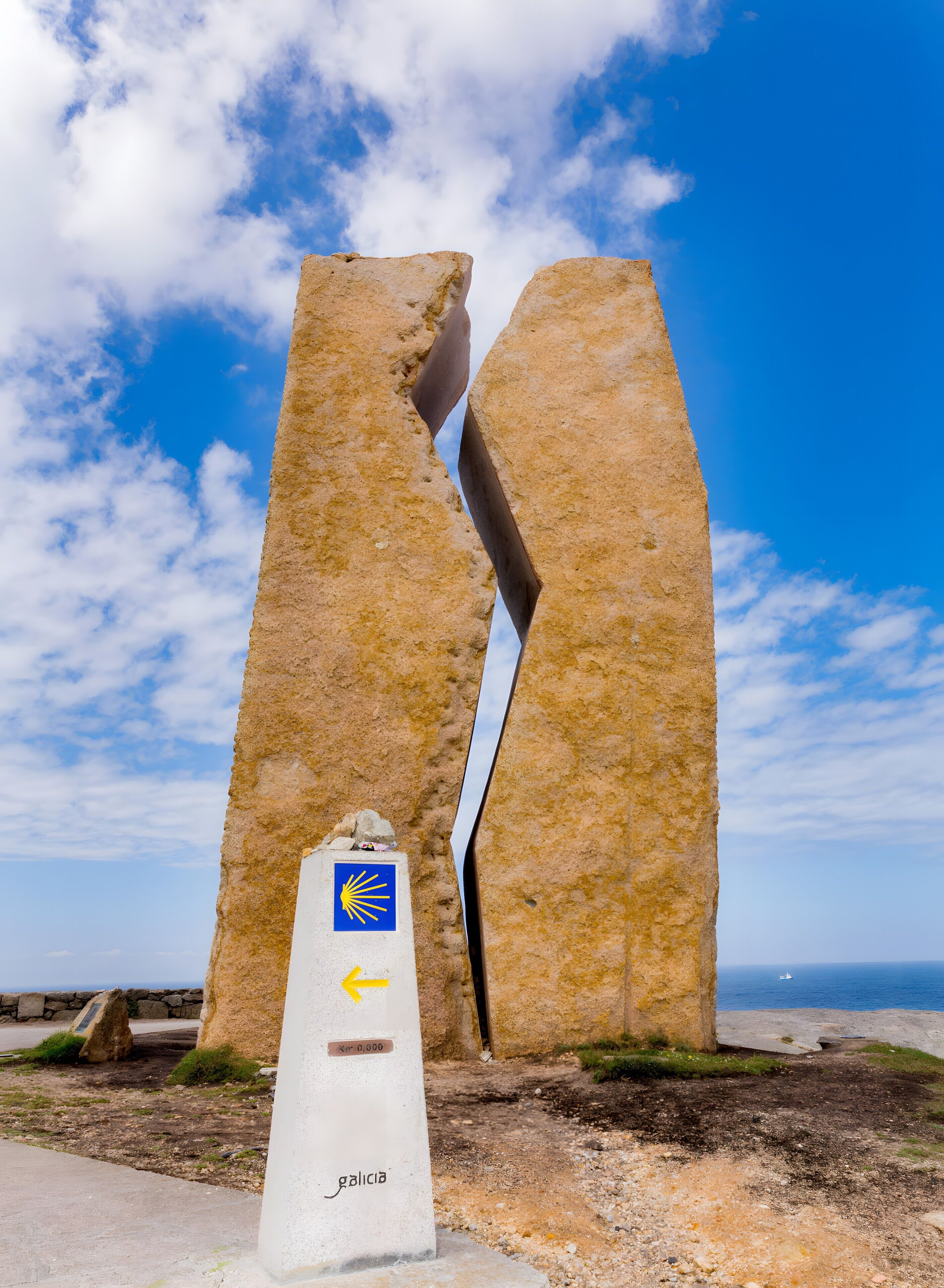 Une grande structure en pierre, avec une enseigne bleue et jaune, un pilier en béton surmonté d’une flèche, et le mot « galice » écrit au sol.