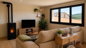 Ein gemütliches Wohnzimmer mit einer Couch, einem Fernseher, einem Kamin, einem Fenster und Blick auf ein Haus.