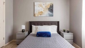 A bedroom with a bed, a nightstand, a lamp, and a wall-mounted abstract painting.