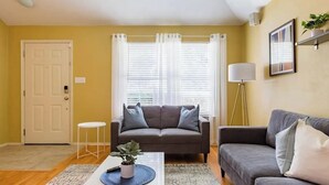 A living room with two sofas, a coffee table, a potted plant, a door, and a window with curtains.