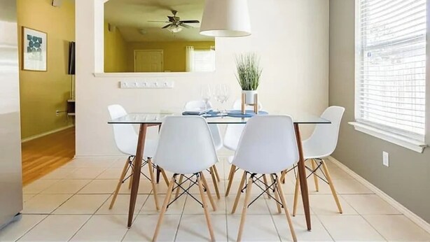 A modern dining area with a glass table, white chairs, and a ceiling fan.