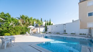 A swimming pool with lounge chairs, a sun umbrella, and a white building with a tiled deck. - Apartment 'Las Palmeras 1' with Shared Pool, Wi-Fi and Air Conditioning (Cala Millor)
