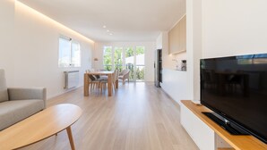 A modern living room with a flat-screen TV, a dining area with chairs, and a sofa. - Apartment 'Las Palmeras 1' with Shared Pool, Wi-Fi and Air Conditioning (Cala Millor)