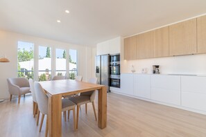 A modern kitchen with white cabinets, a wooden dining table, and a large window overlooking a residential area.