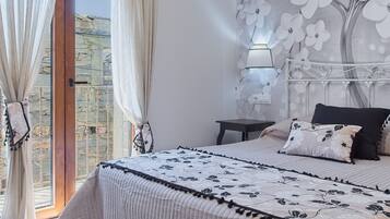 A bedroom with a bed, a nightstand, a wall-mounted lamp, and a view of a stone wall through a glass door.