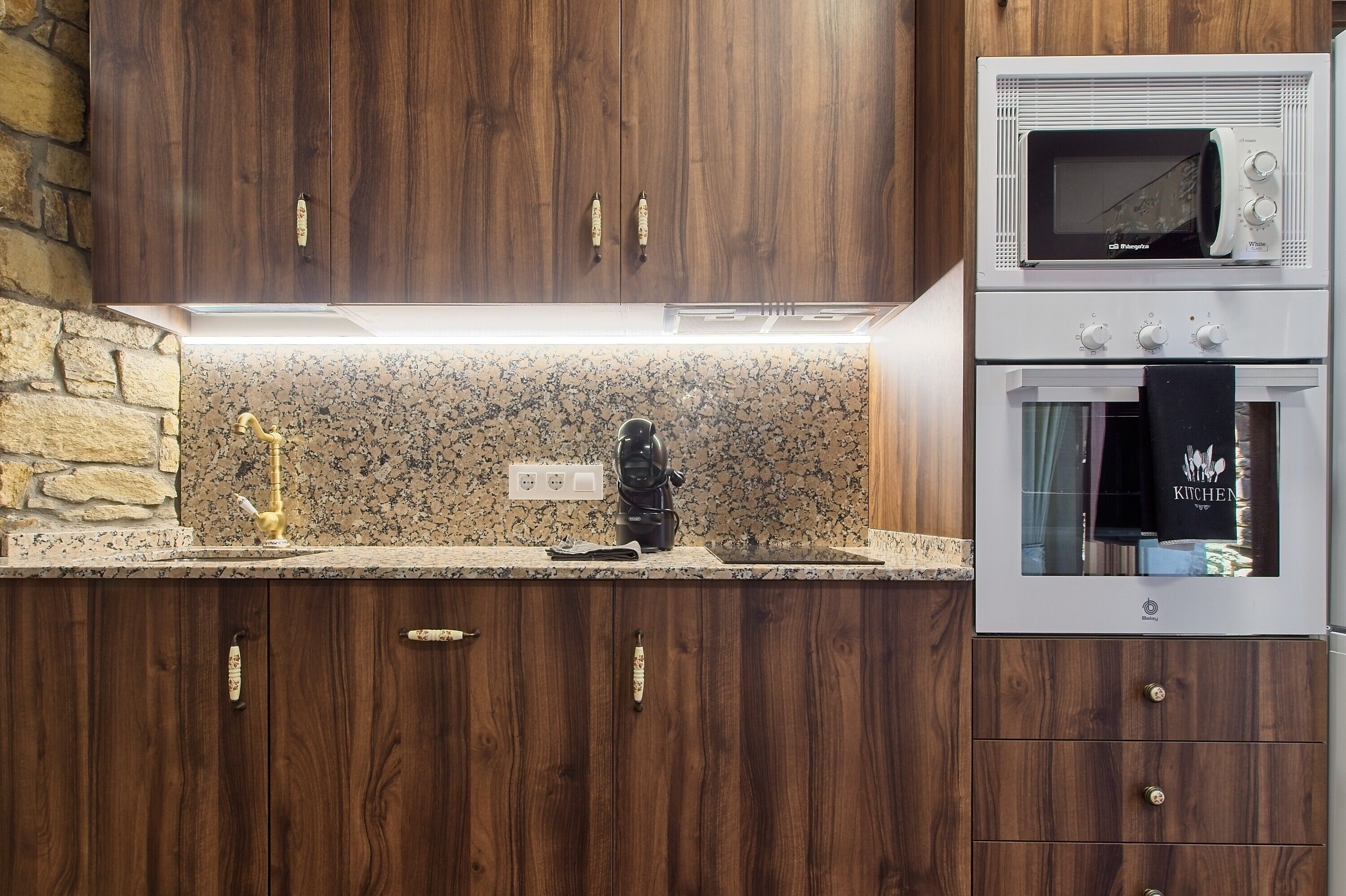 A kitchen with wooden cabinets, a granite countertop, a coffee maker, a microwave, and an oven.