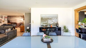 A modern living room with a glass coffee table, grey sofa, and a cityscape painting on the wall. - Chambre d’hôtes Chêne with Air Conditioning – Serenity, Nature and Well-being in Gascony (Mauléon-d'Armagnac)