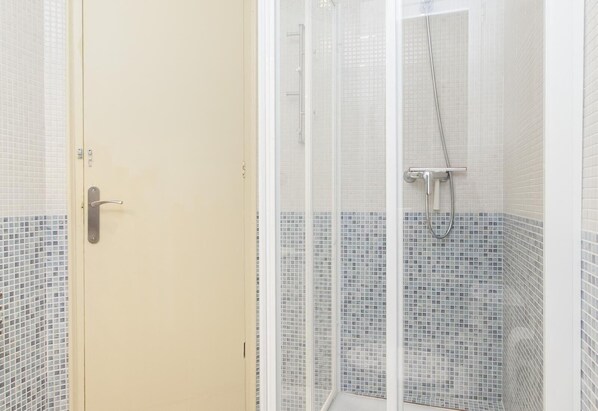 Un baño con ducha, paredes con azulejos y una puerta.