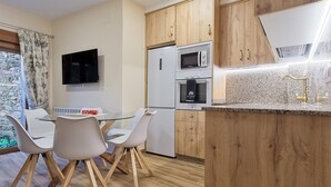 A modern kitchen with wooden cabinets, a built-in microwave, a refrigerator, and a glass dining table with chairs. - Holiday Home 'Lago De Sanabria' with Mountain View, Private Garden and Balcony (Coso)