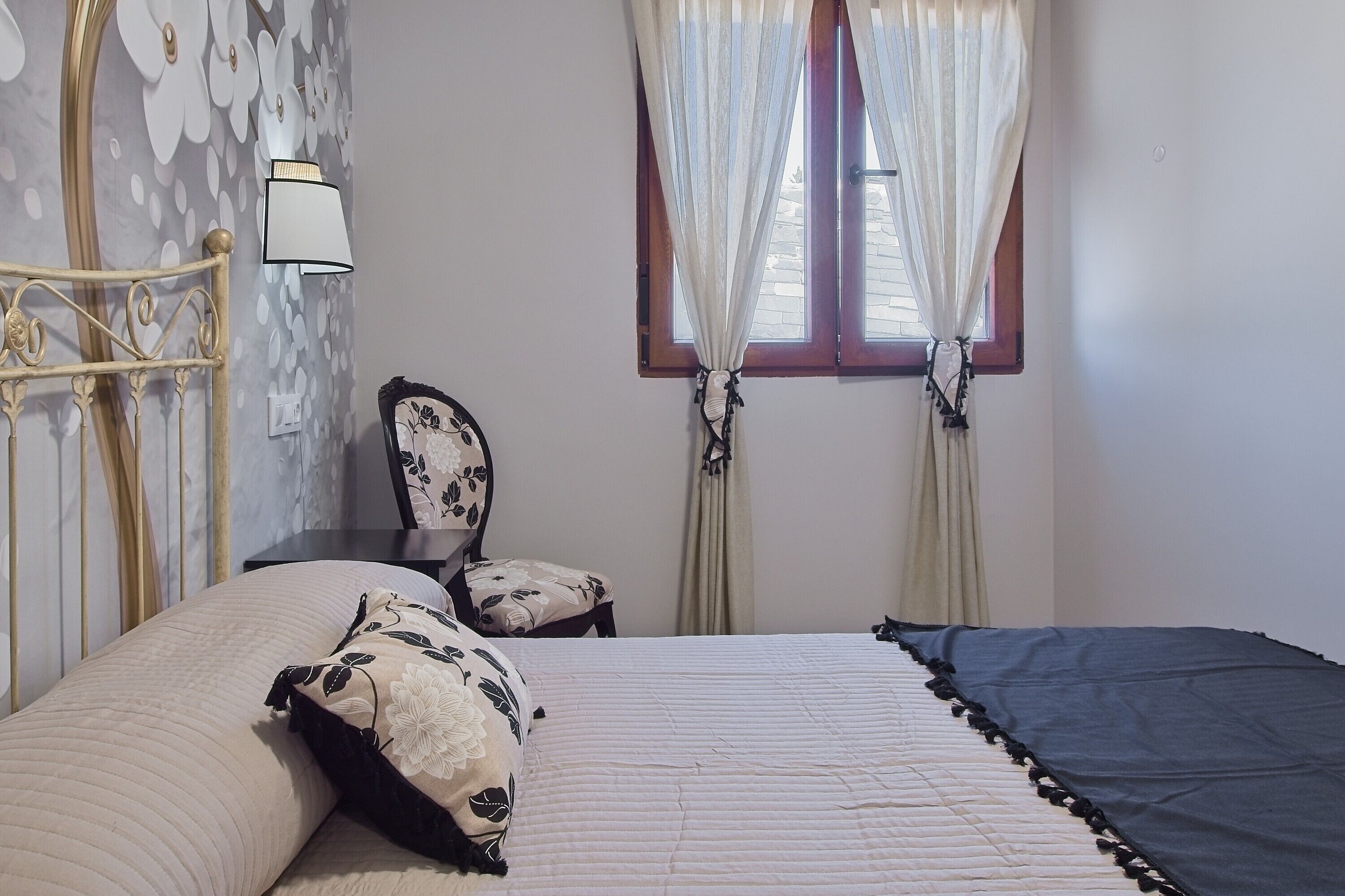 Een slaapkamer met een bed, een stoel, een lamp en een raam met gordijnen.