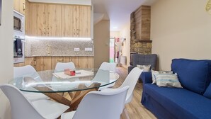 A modern kitchen with wooden cabinets, a glass-top dining table, white chairs, and a blue sofa. - Holiday Home 'Lago De Sanabria' with Mountain View, Private Garden and Balcony (Coso)